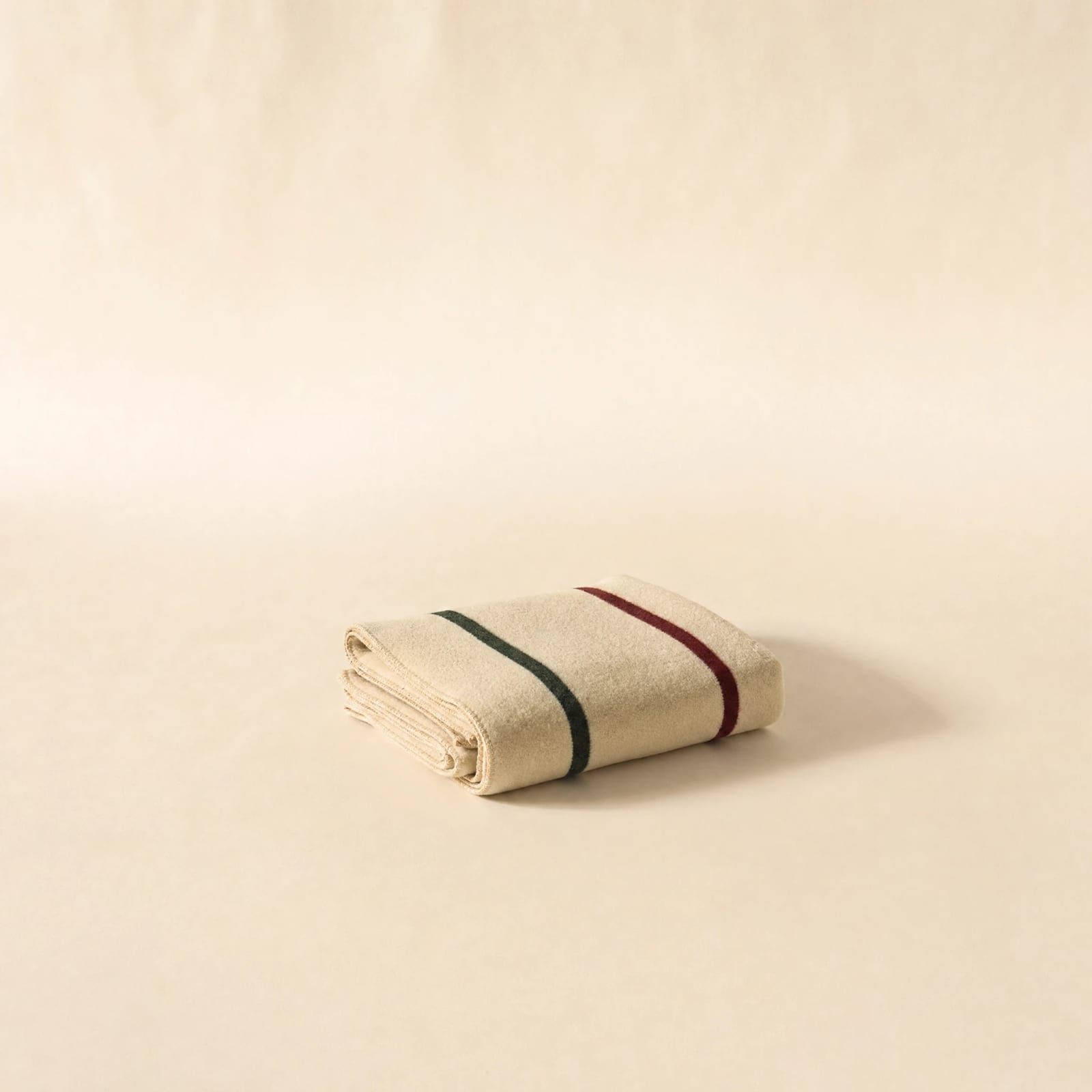 No. 02 Camp Blanket — folded cream merino wool with oxblood and forest-green point stripes